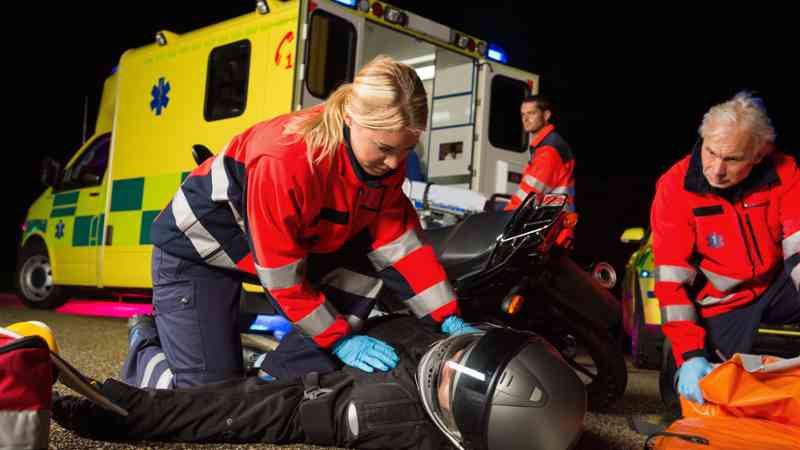 Paramédicos atendiendo a motorista caído junto a ambulancia — formación para el empleo