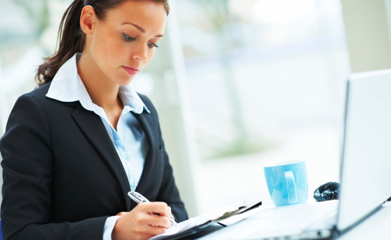 Mujer profesional tomando notas junto a un portátil y una taza — cursos online