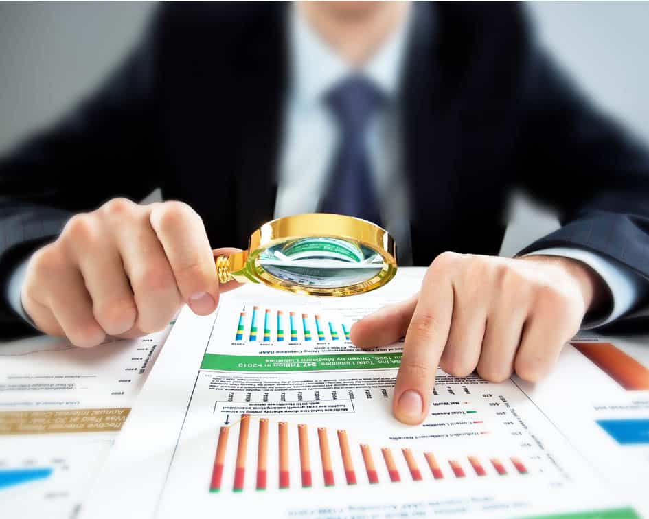 Manos examinando gráficos financieros impresos con lupa, señalando un dato — cursos online