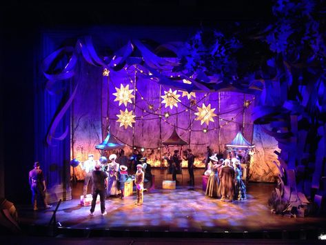 Escena teatral iluminada con actores en vestuario de época y decorado de mercado, cursos online