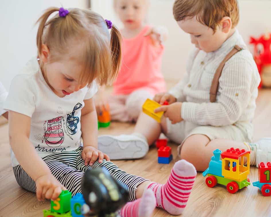 Niños pequeños jugando con bloques y tren de juguete en suelo de madera — cursos online