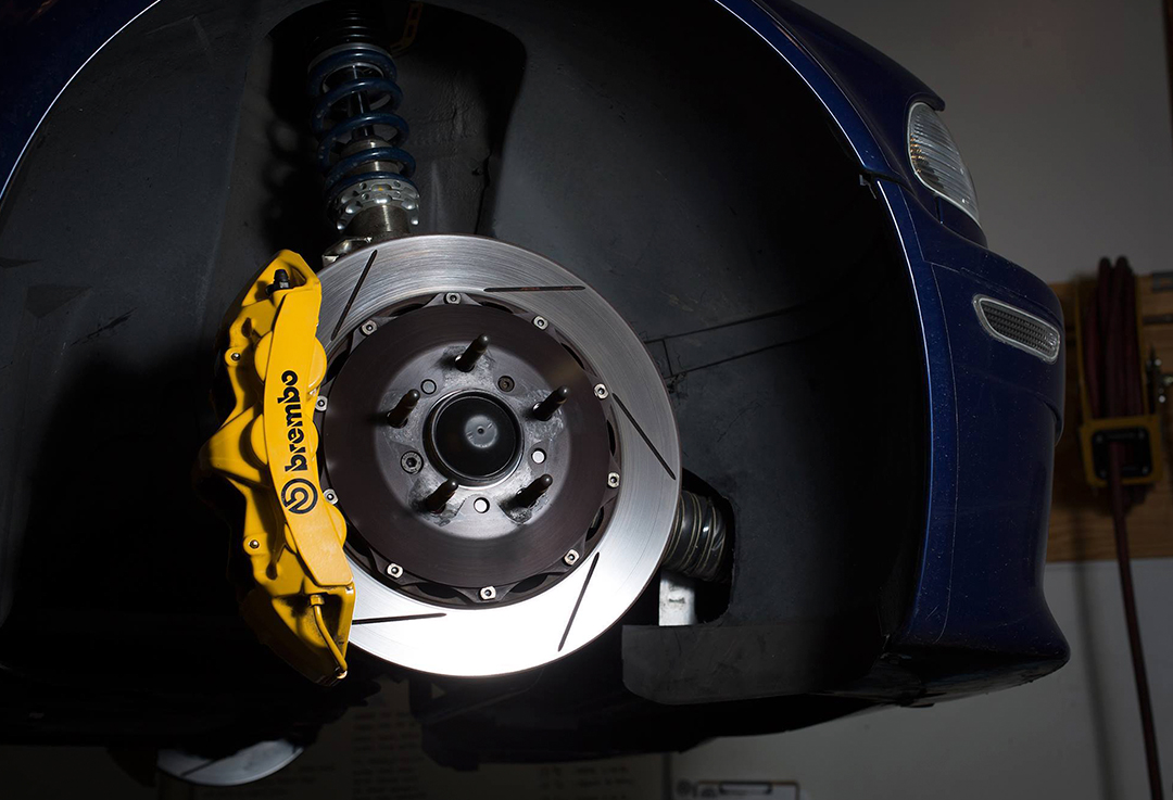 Pinza de freno Brembo amarilla y disco de freno en coche elevado, mecánico industrial