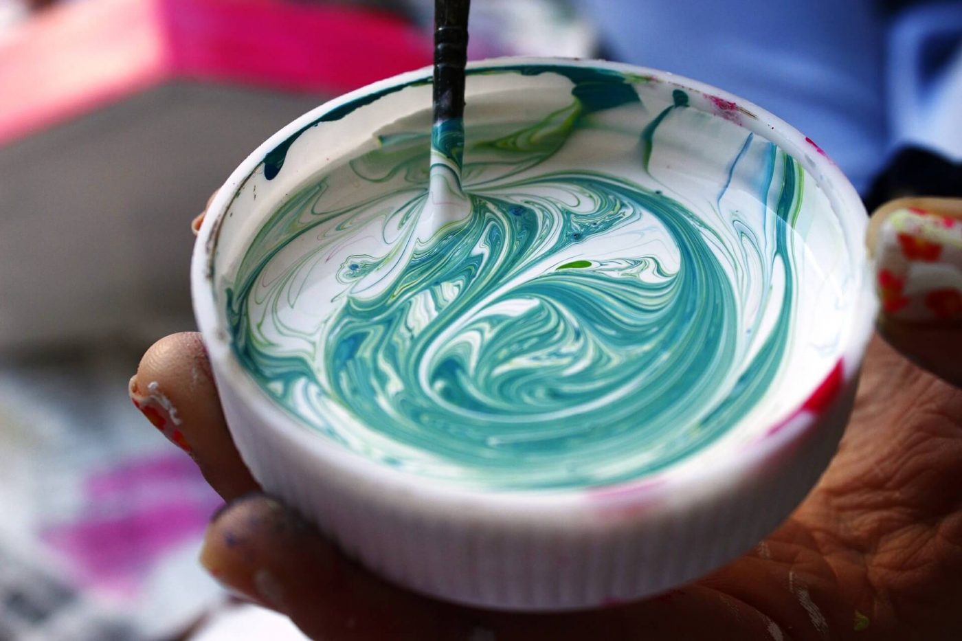 Tapa con pintura blanca y verde en remolinos agitada con un palillo, sostenida por una mano — formación para el empleo