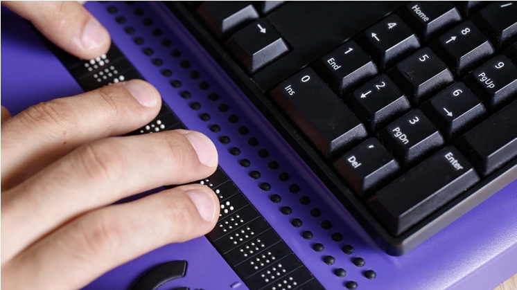 Manos leyendo un display braille junto a un teclado de ordenador — cursos online