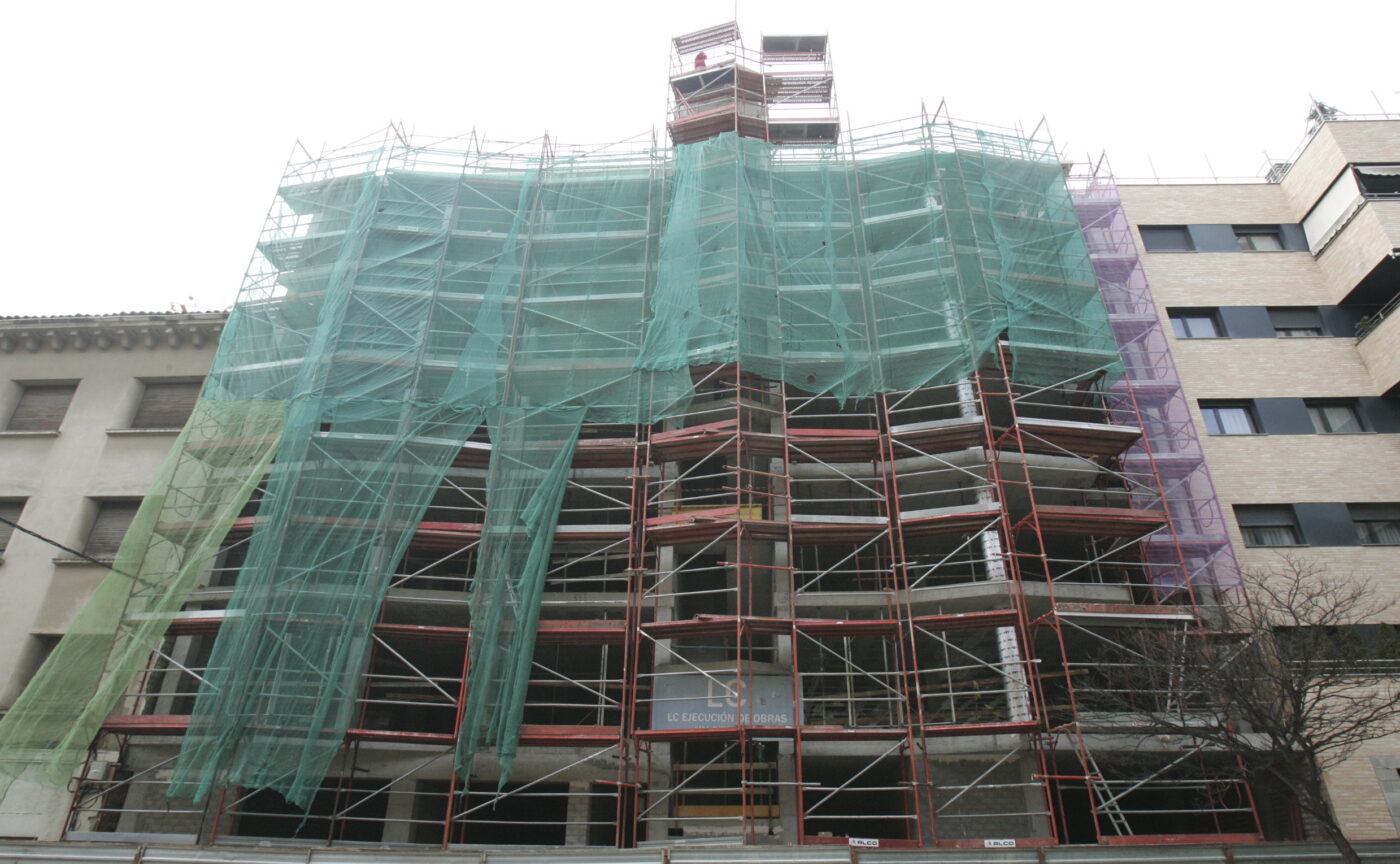 Andamio con malla protectora en fachada de edificio en obras, cursos sector industrial