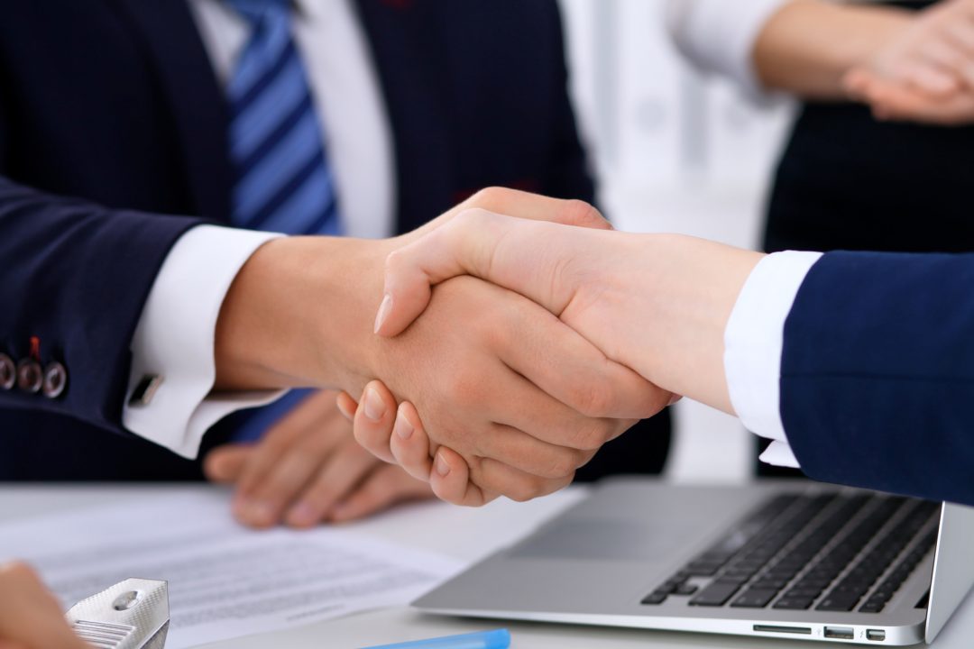 Apretón de manos entre dos profesionales sobre mesa con portátil y documentos — formación para el empleo