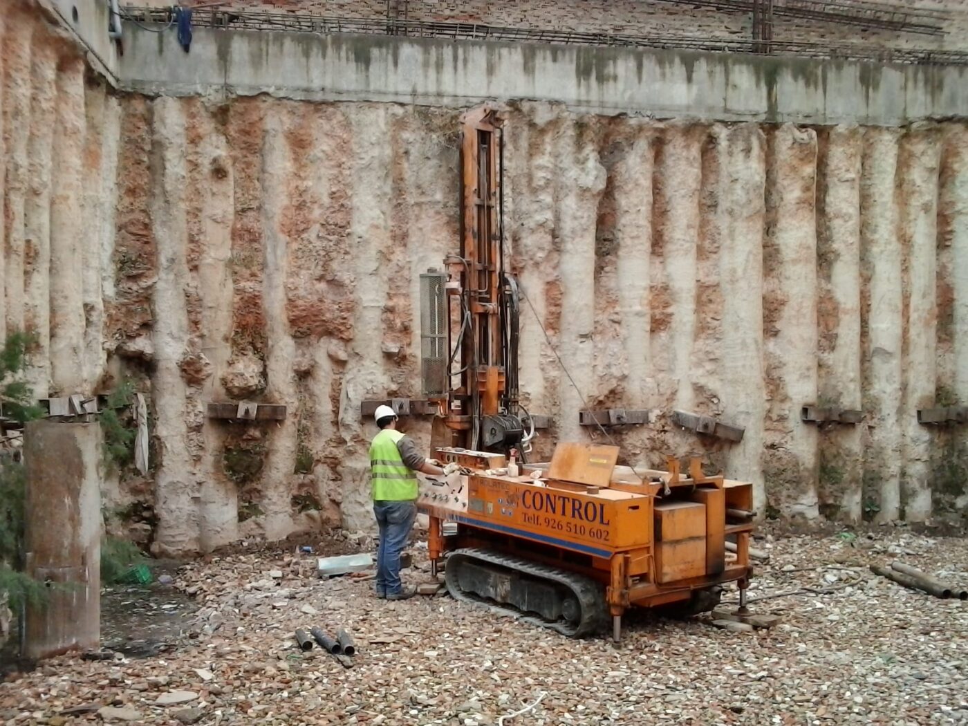 Operario con chaleco y casco junto a perforadora sobre orugas en excavación, cursos de maquinaria