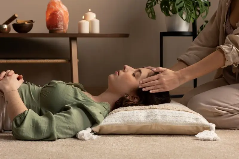 Mujer recostada recibiendo terapia holística con manos del terapeuta en la frente, formación a medida