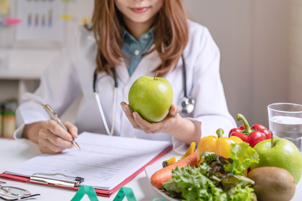 Nutricionista con manzana, verduras y ficha de consulta — cursos online