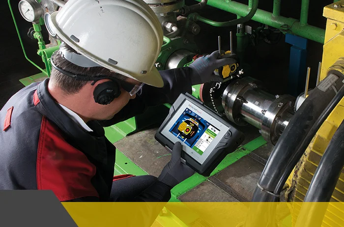 Técnico con casco y tablet inspeccionando un acoplamiento de máquina para mantenimiento industrial