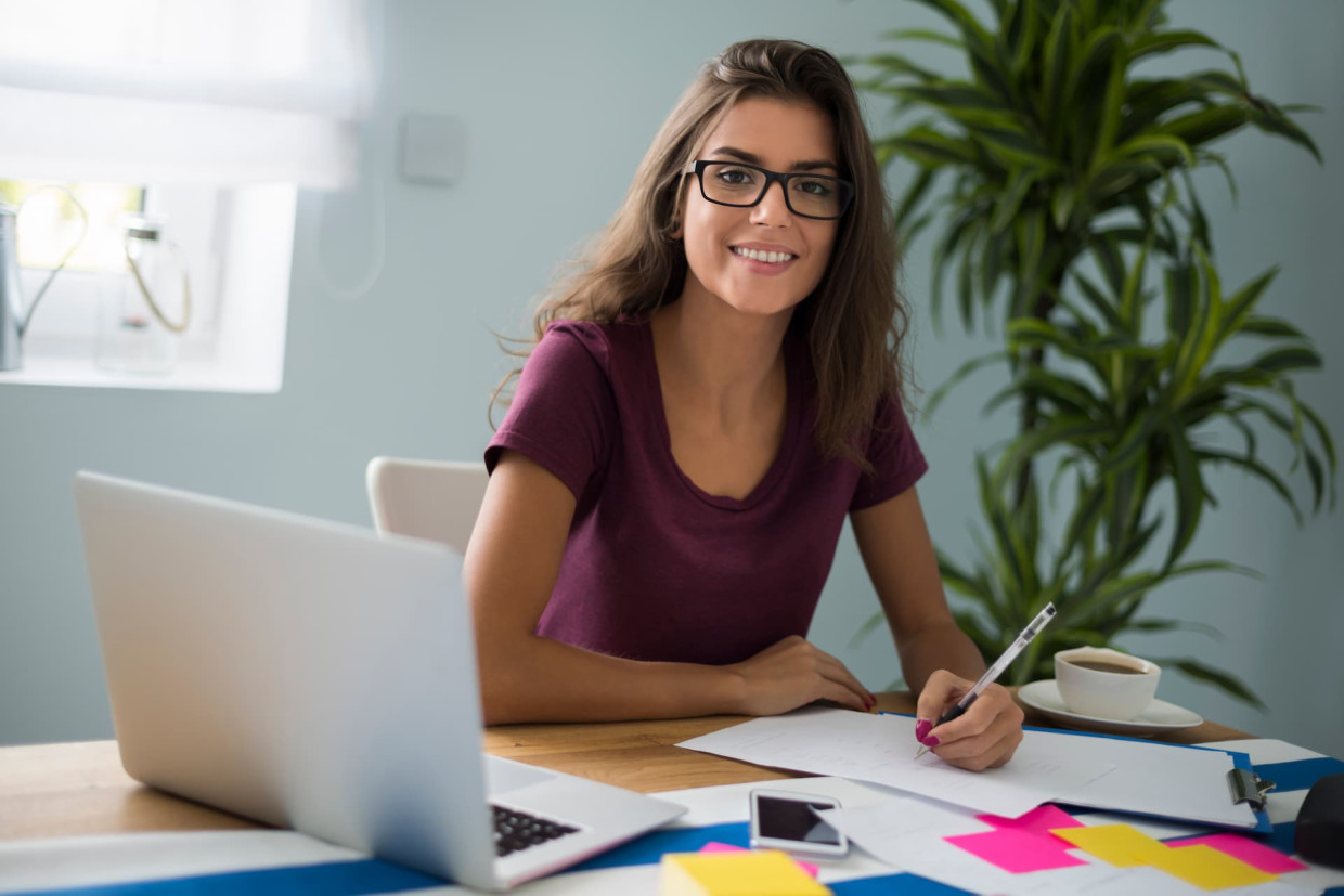 Joven trabajando en escritorio con portátil y apuntes, cursos online