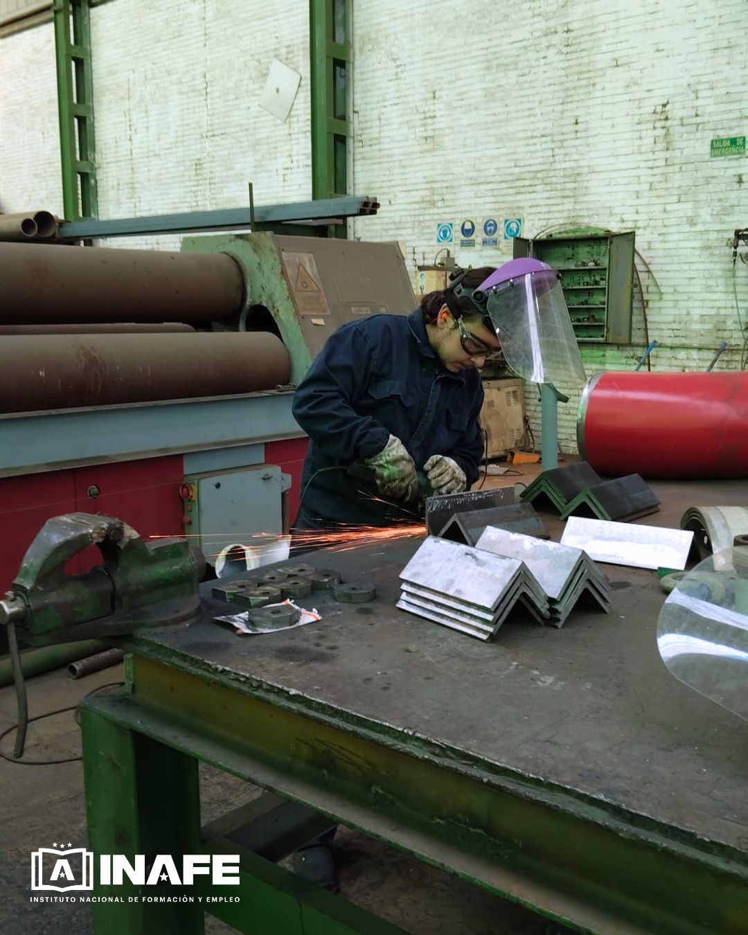 Operario con pantalla facial y guantes lijando piezas en calderería industrial