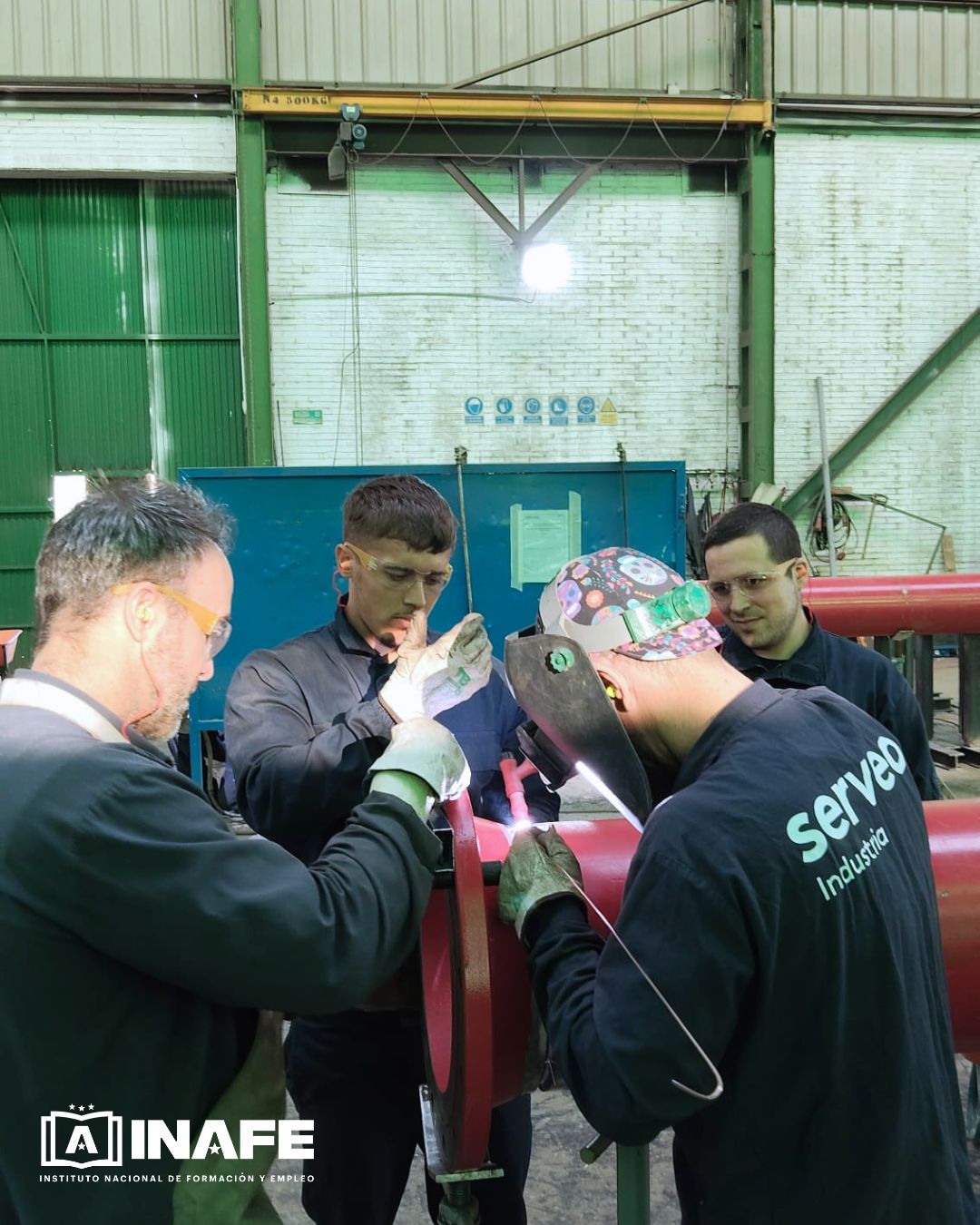 Operario tubero soldando una brida met&aacute;lica roja en taller industrial