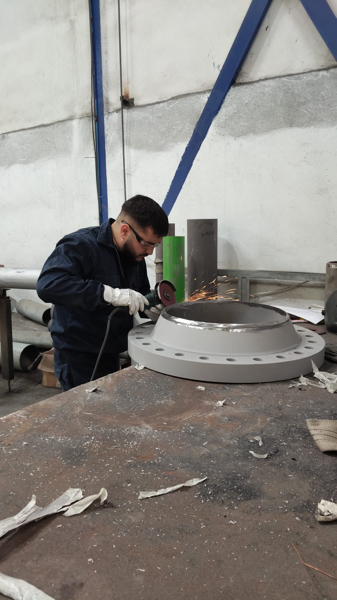 Operario con amoladora desbastando una brida metálica, calderería industrial