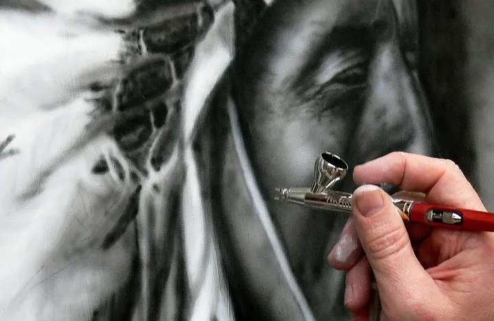 Mano con aerógrafo pintando un retrato en blanco y negro — cursos con prácticas en empresa