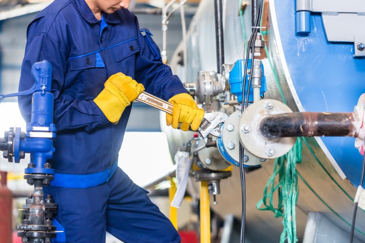 Técnico con mono azul y guantes amarillos ajustando una válvula con llave en un equipo de mantenimiento industrial