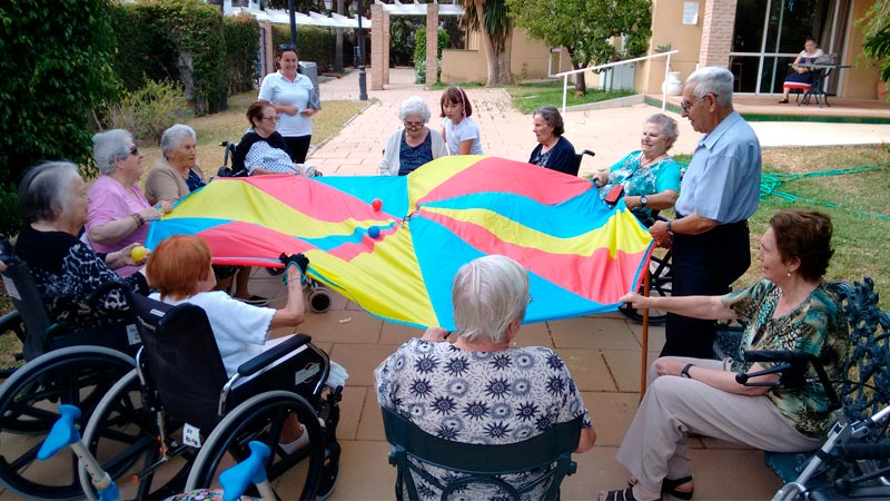 Personas mayores en círculo sosteniendo un paracaídas multicolor — formación para asociaciones