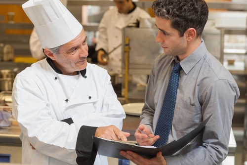 Chef y hombre con carpeta conversan en cocina profesional — formación para el empleo