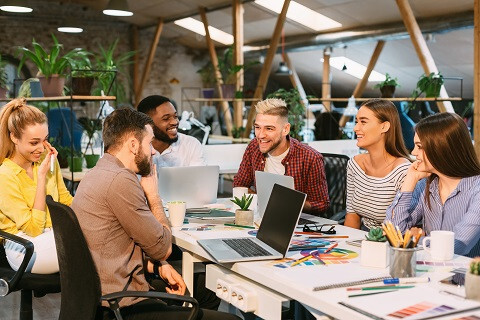 Equipo joven en oficina abierta alrededor de una mesa con portátiles y material de trabajo, formación para el empleo