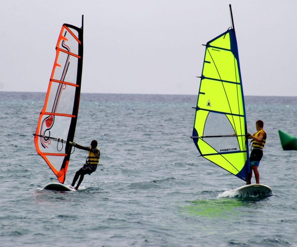 Dos windsurfistas con chalecos y velas naranja y amarilla en el mar — cursos en Huelva