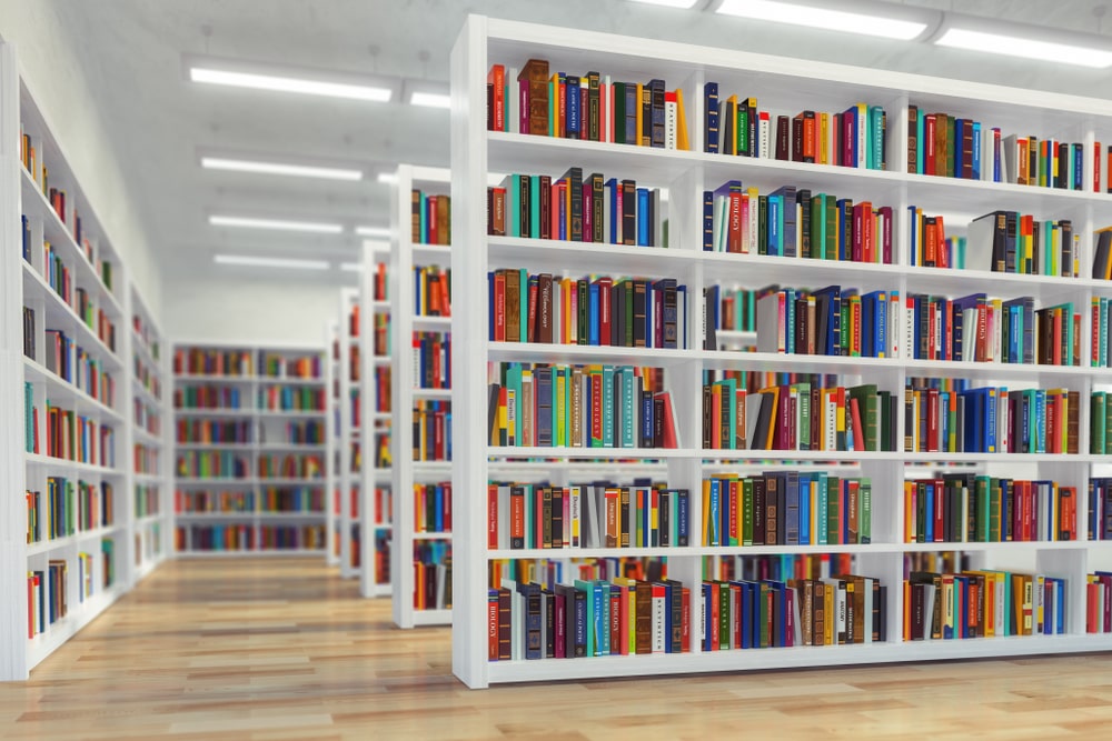 Estanterías blancas repletas de libros en biblioteca, formación para el empleo