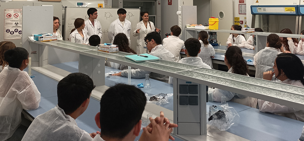 Laboratorio docente con estudiantes en batas blancas y profesores al frente, formación para el empleo