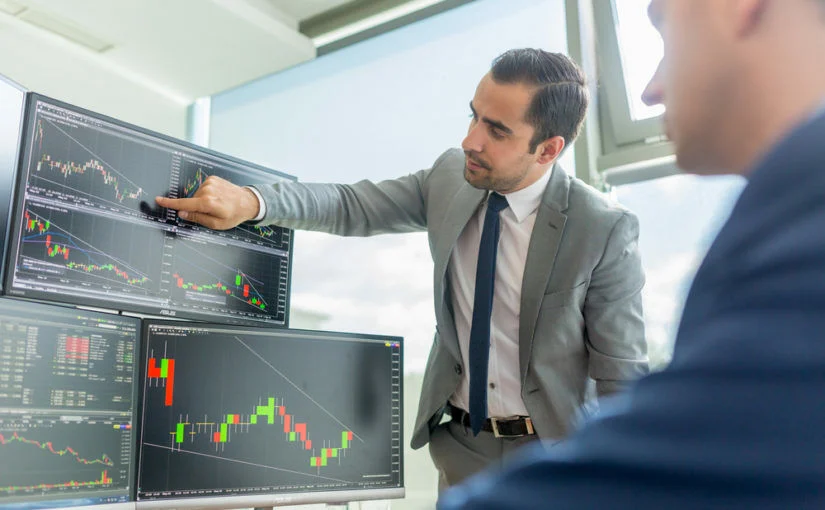 Hombre señalando gráficos bursátiles en varios monitores (cursos online)