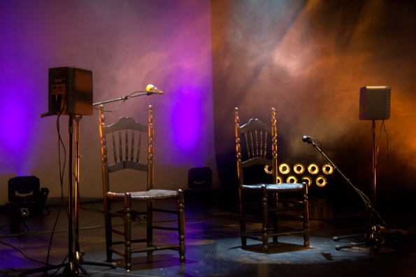 Escenario vacío con dos sillas de madera, micrófonos y altavoces — cursos online