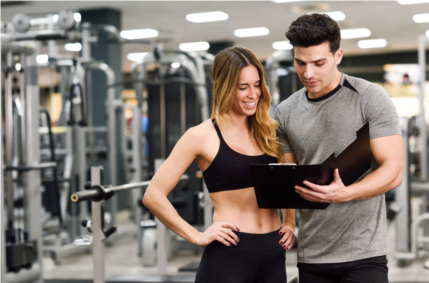Entrenador mostrando una carpeta a una clienta en gimnasio — formación a medida