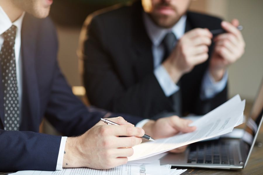 Dos profesionales en traje revisando documentos y portátil, formación para el empleo