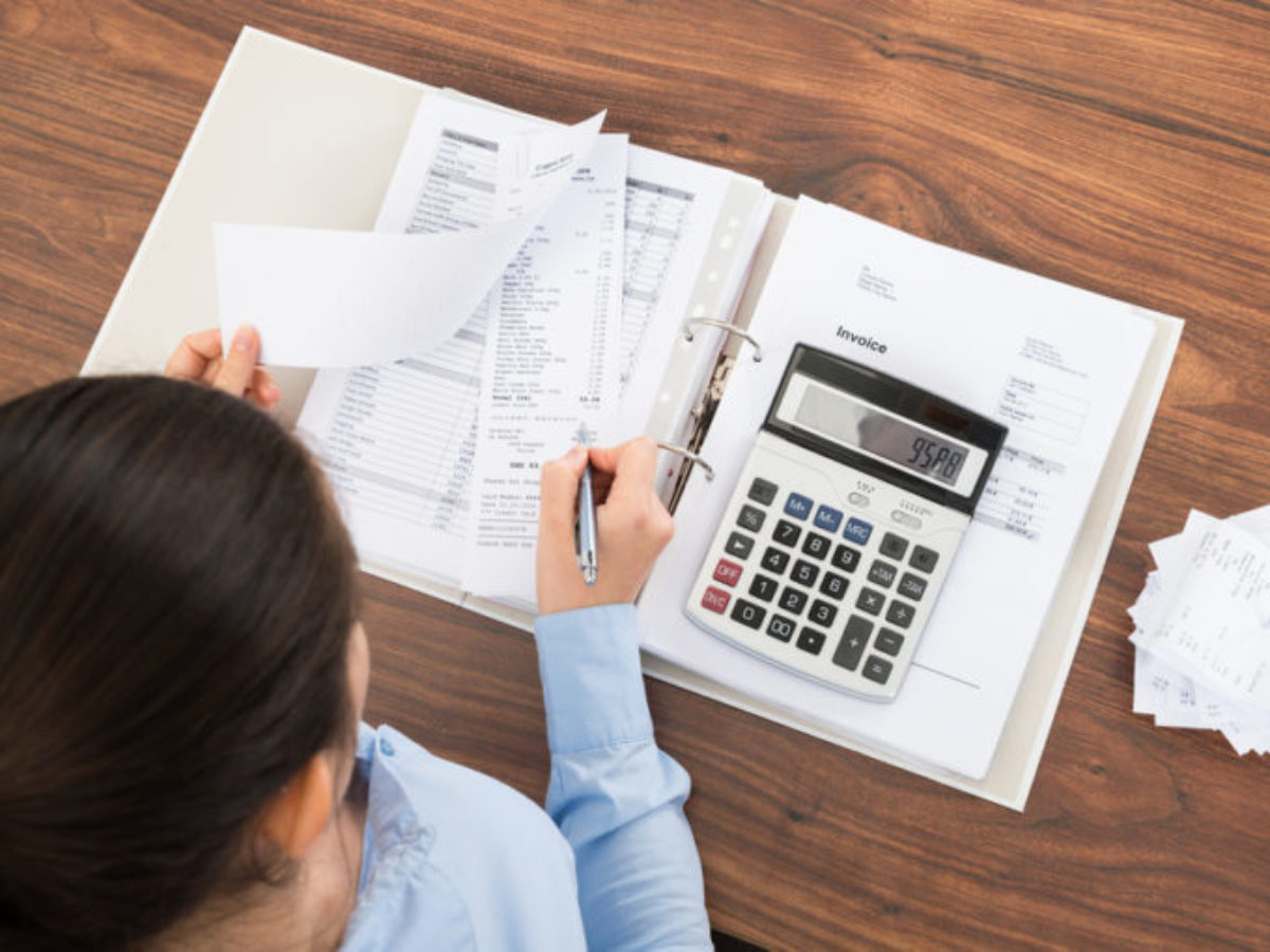 Persona revisando facturas y anotaciones en una carpeta con calculadora — cursos online