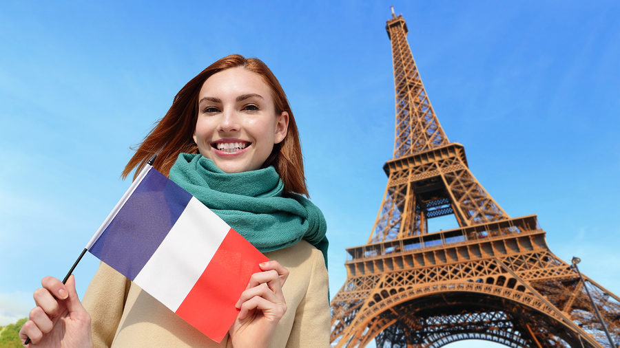 Mujer sonriente con bandera francesa frente a la Torre Eiffel, cursos online