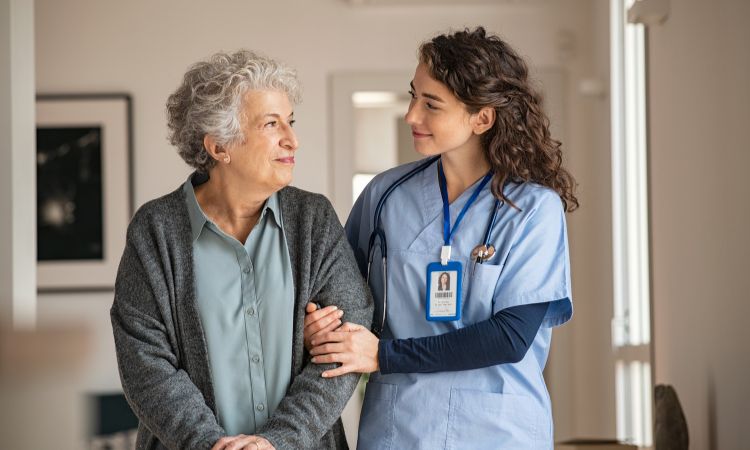 Cuidadora con uniforme azul sujetando el brazo de una mujer mayor, formación para el empleo