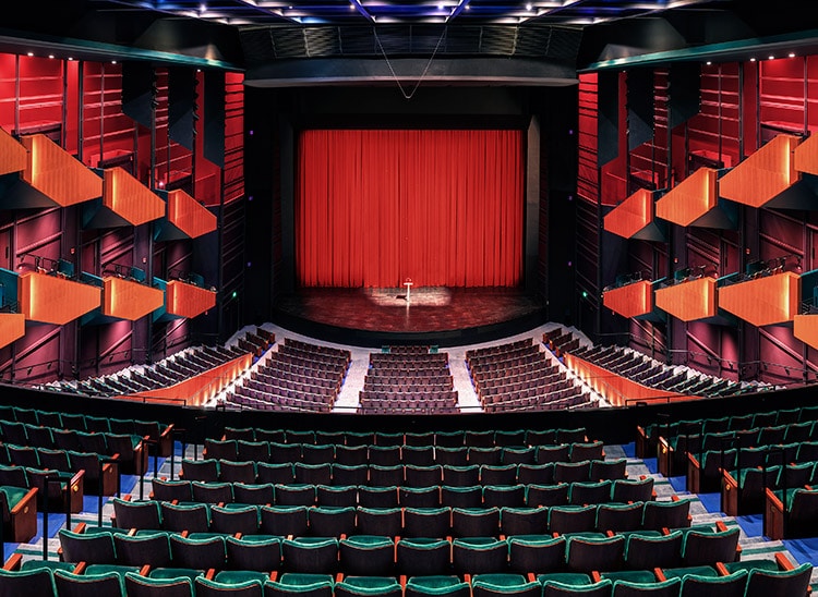 Auditorio vacío con escenario, cortina roja y micrófono en el centro; formación para el empleo