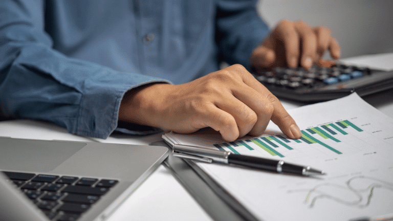 Mano señalando gráfico impreso junto a portátil y calculadora — cursos online
