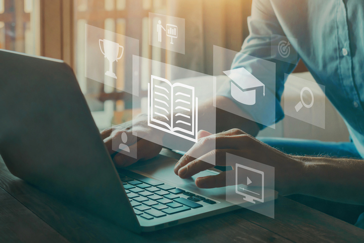 Manos tecleando en un portátil con iconos educativos flotantes, cursos online