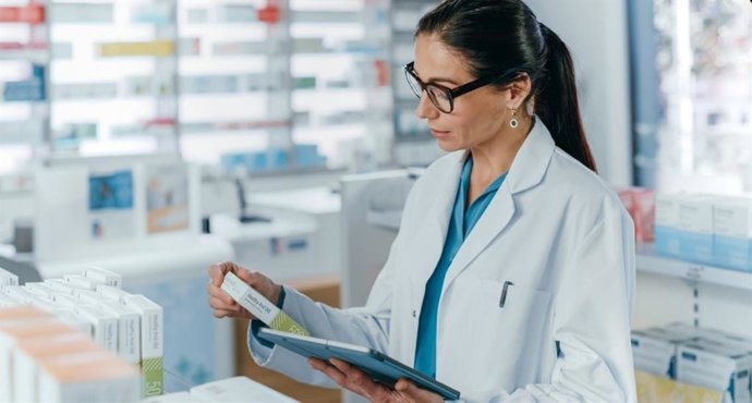 Farmacéutica con bata y tablet revisando un medicamento — formación para el empleo