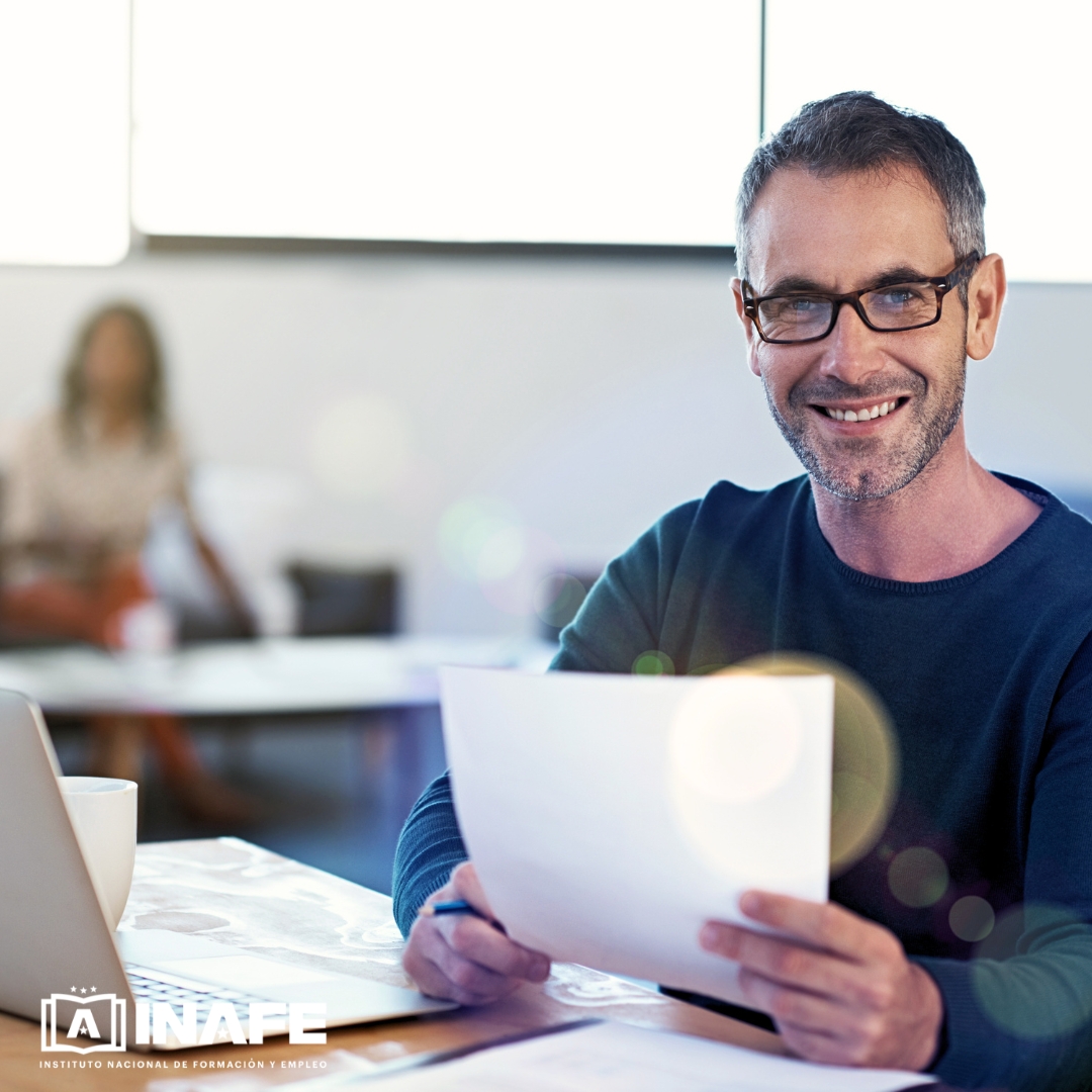 Hombre con gafas sosteniendo papeles en escritorio, formaci&oacute;n para el empleo