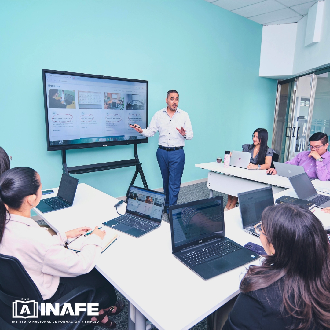 Formador explicando ante pantalla digital con asistentes y portátiles — formación para el empleo