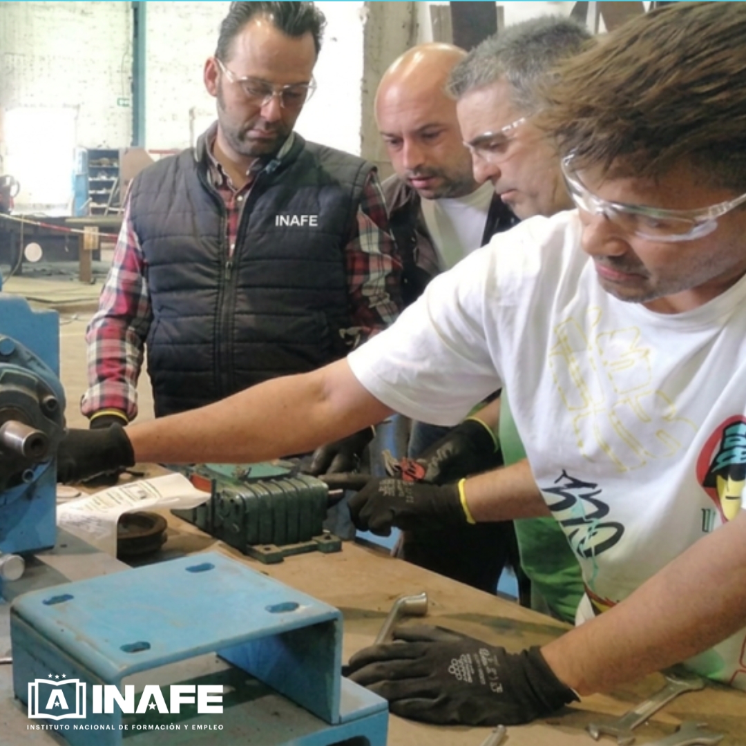 Operario mecánico industrial con gafas y guantes manipulando maquinaria en taller