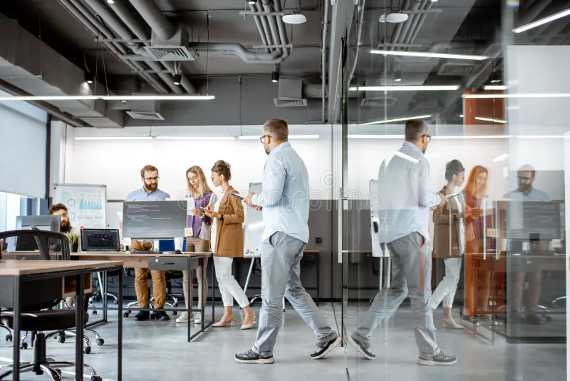 Personas en oficina colaborando junto a pantallas y pizarra, formación para el empleo