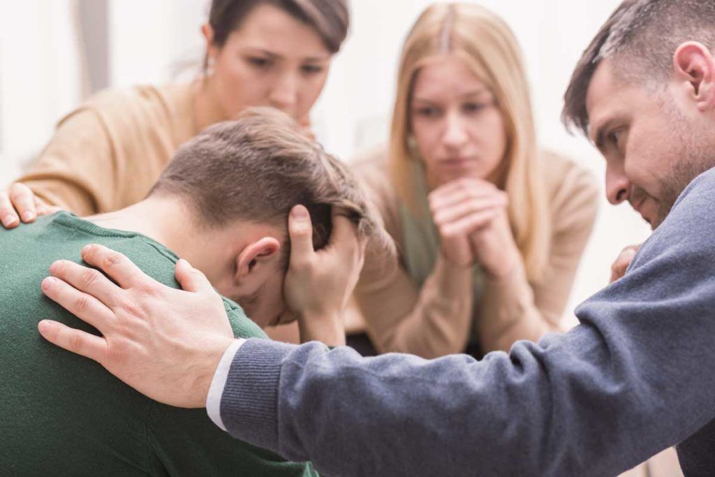 Hombre con la cabeza entre las manos consolado por tres personas, formación para asociaciones
