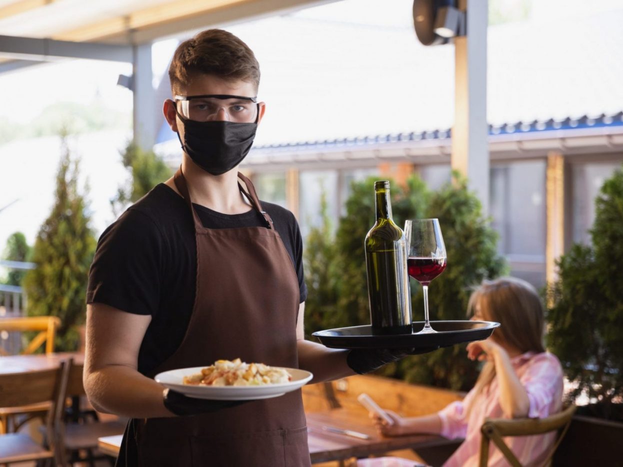 Camarero con mascarilla, gafas protectoras y guantes sirviendo plato y copa de vino — cursos online