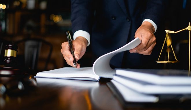 Manos firmando documentos legales en un escritorio con mazo y balanza — formación para administraciones públicas