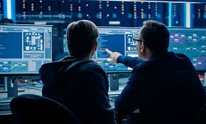 Persona señalando pantalla a otra en sala de control — formación para el empleo