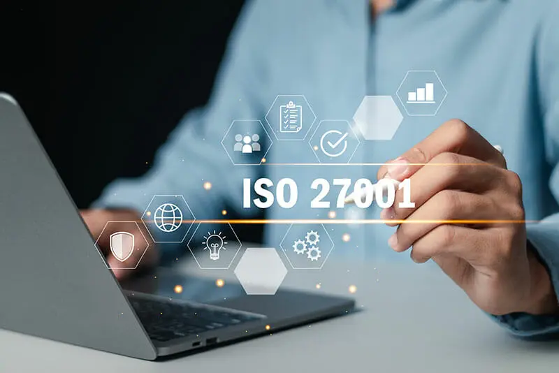Mano junto a portátil con texto 'ISO 27001' y iconos digitales, cursos online
