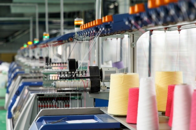Máquina textil industrial con conos de hilo rosa y amarillo (cursos sector industrial)