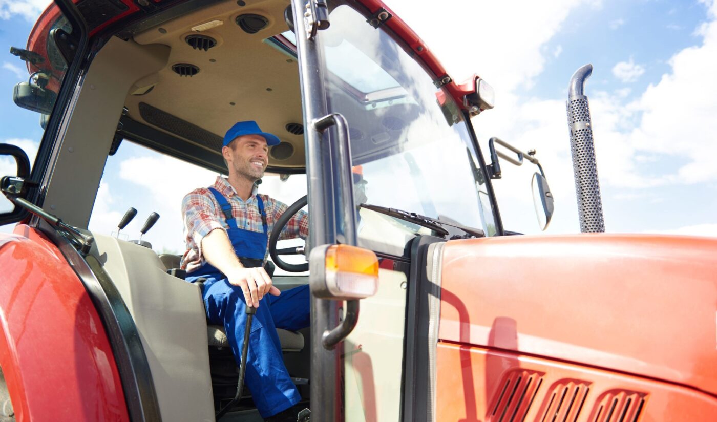 Hombre con peto y gorra azules en la cabina de un tractor rojo