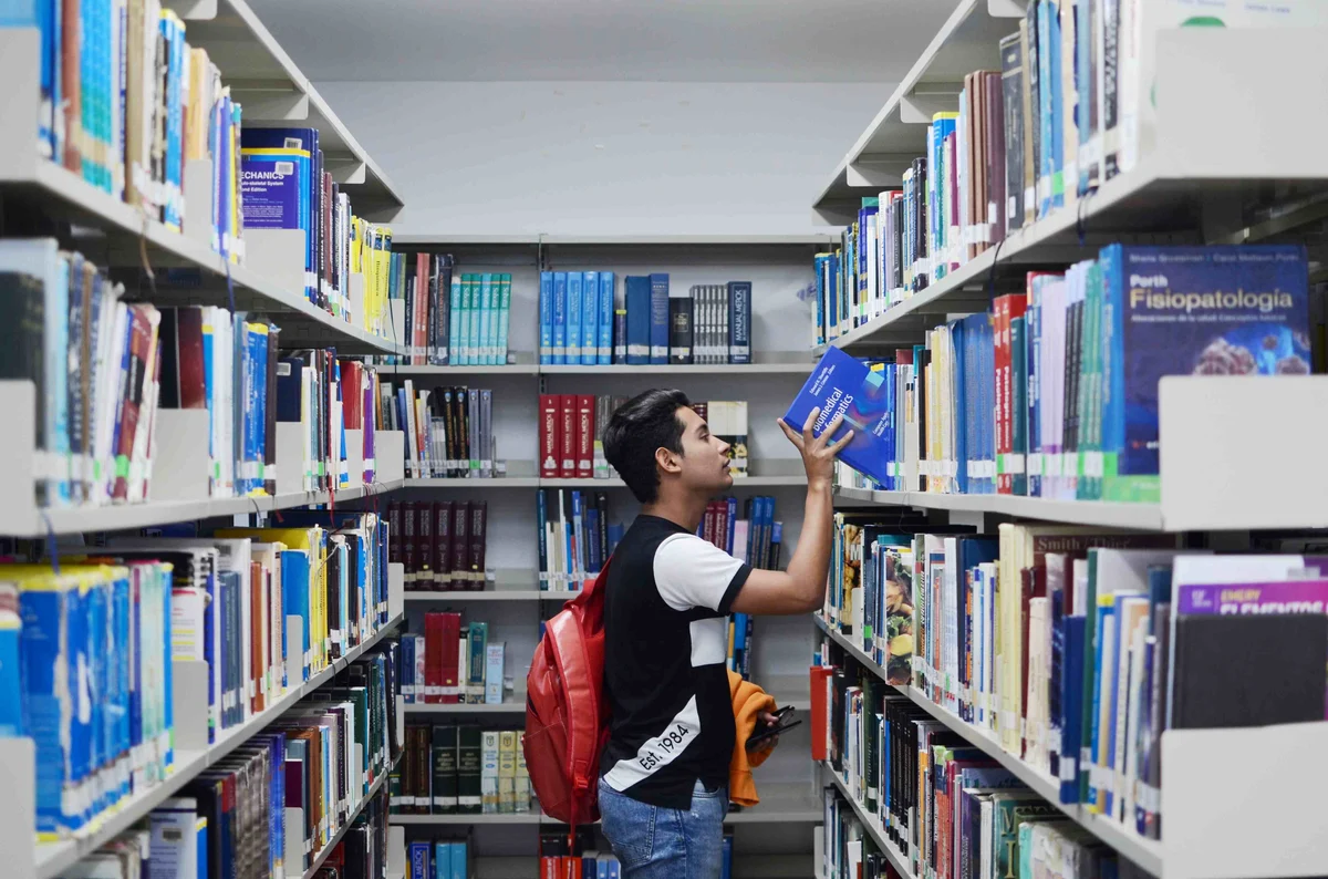 Estudiante en biblioteca buscando un libro, formación para el empleo