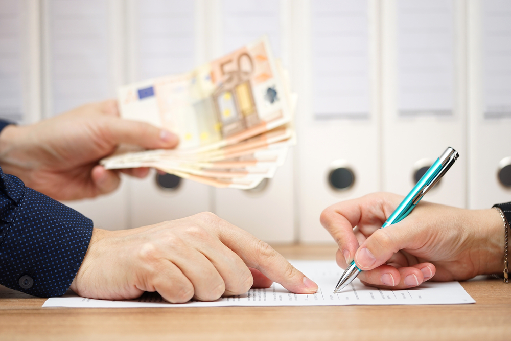 Manos firmando un documento mientras se entregan billetes — formación para el empleo
